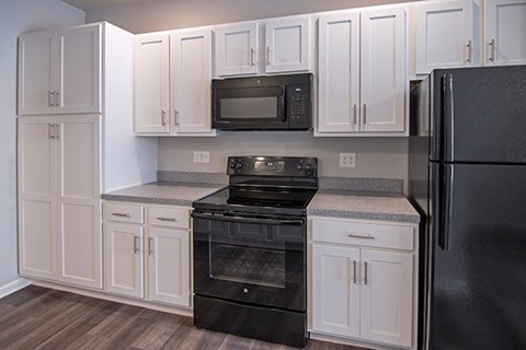 A black refrigerator sits next to a black oven and microwave in a kitchen.