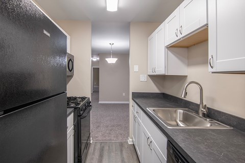 A black refrigerator is in a kitchen with white cabinets.