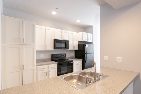 A kitchen with white cabinets and a black microwave.