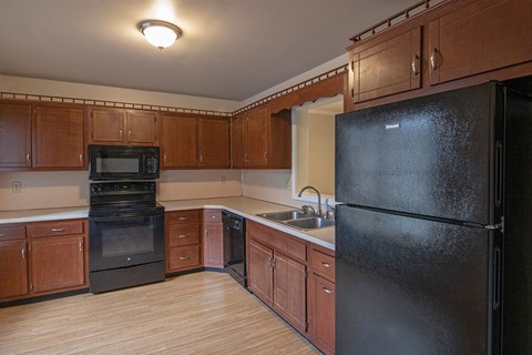 A black refrigerator is in the corner of a kitchen with wooden cabinets.