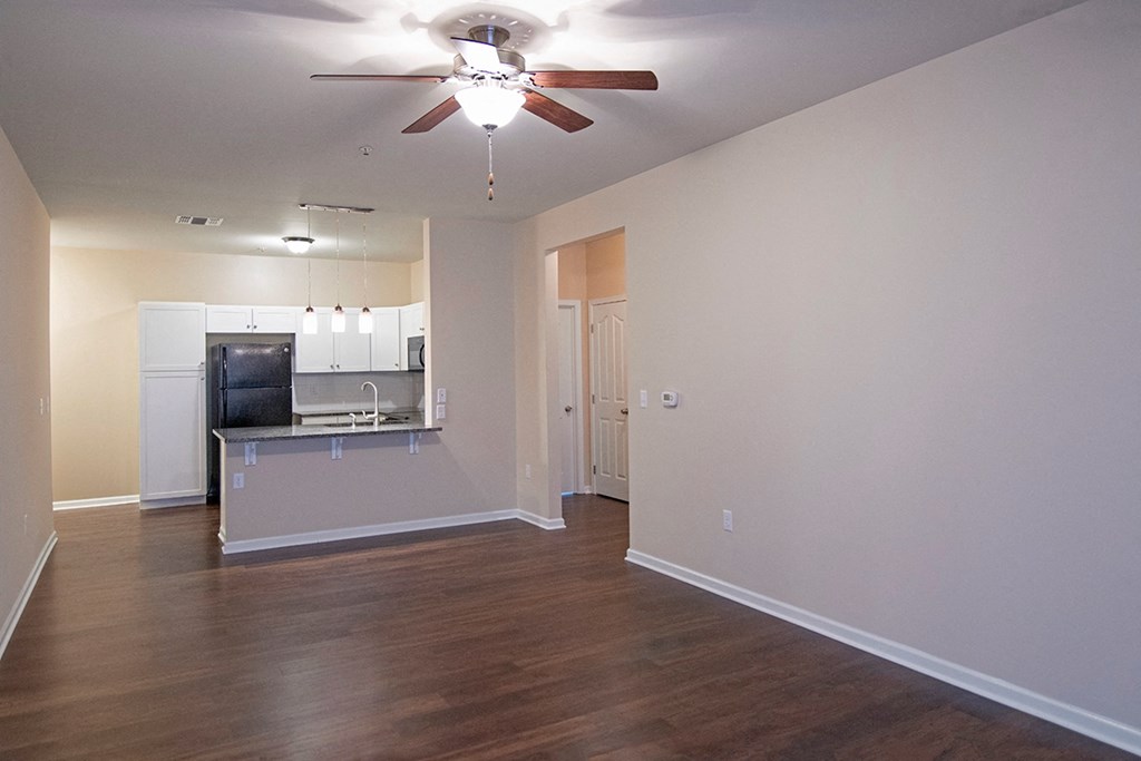 an empty living room with a ceiling fan and a kitchen