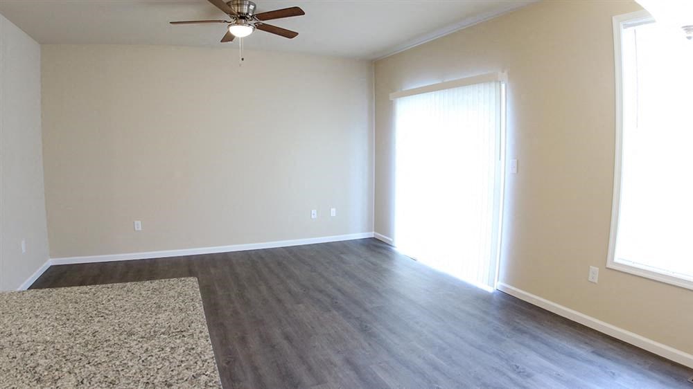 an empty living room with wood floors and a ceiling fan