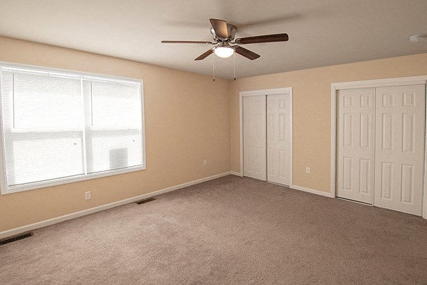 an empty living room with a ceiling fan and two windows