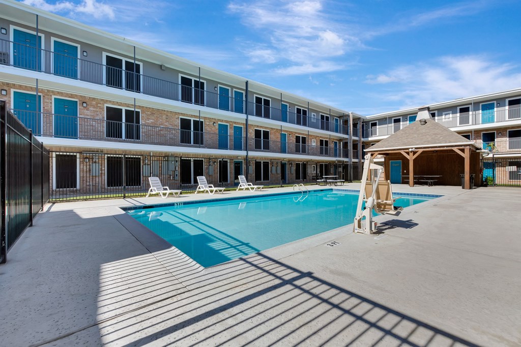 A swimming pool is surrounded by sun loungers in front of a building.