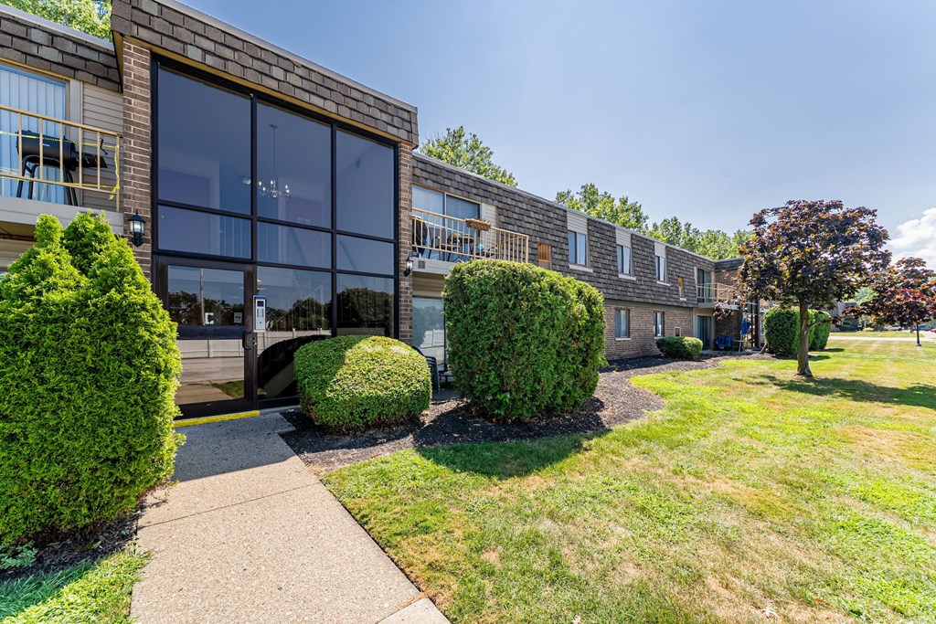 A building with a glass facade is surrounded by green bushes and trees.