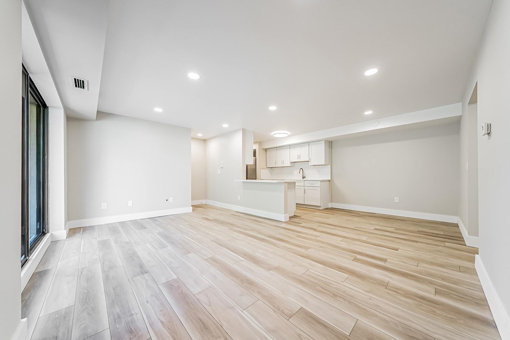 A spacious room with wooden flooring and a kitchenette in the background.