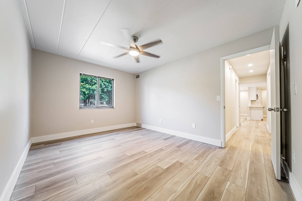 A room with a ceiling fan and a window with a view of trees.