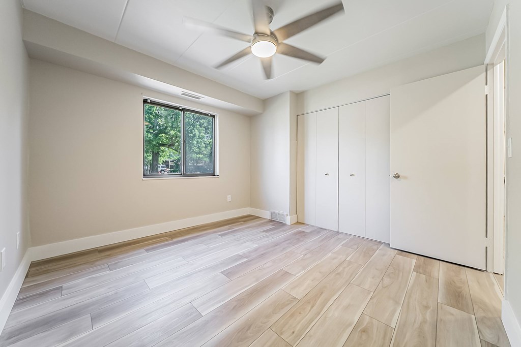 A room with a ceiling fan and a window with a view of trees.