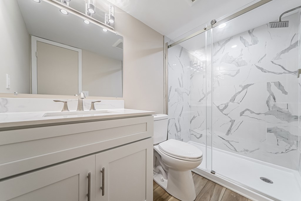 A white toilet sits in a bathroom with a marble shower wall.