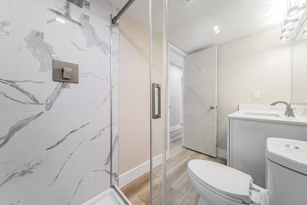 A bathroom with a marble tile shower and a white toilet.