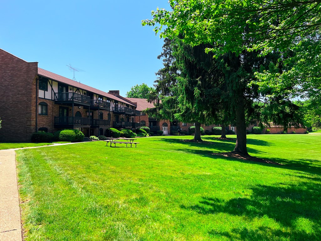a grassy area with trees and a picnic table in front of a brick building