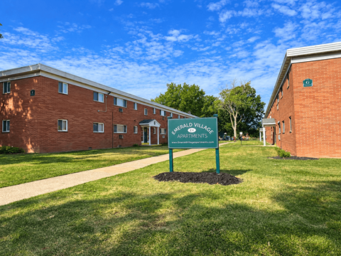 A green sign in front of a brick building that says Berkley Village Apartments.