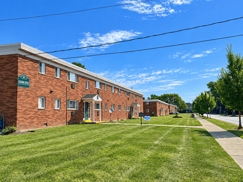 A long brick building with a green sign in front.