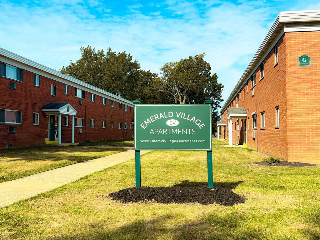 A sign for Emarald Village Apartments stands in front of a brick building.