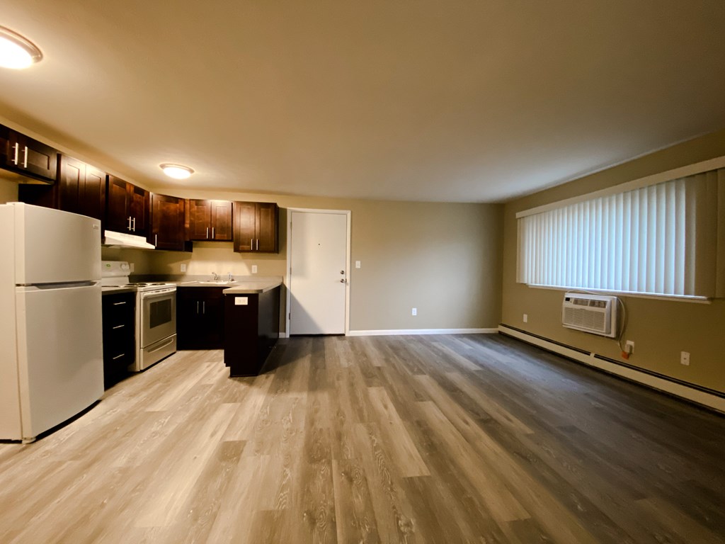 an empty kitchen and living room with plank flooring and white appliances