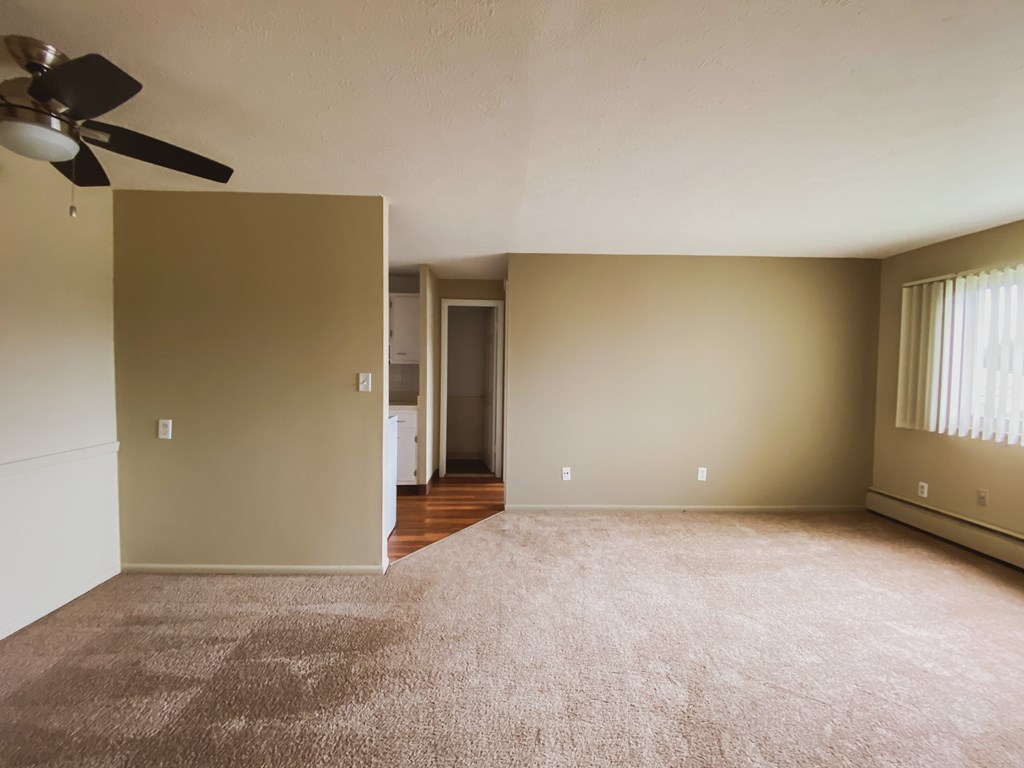 an empty living room with a ceiling fan and carpet