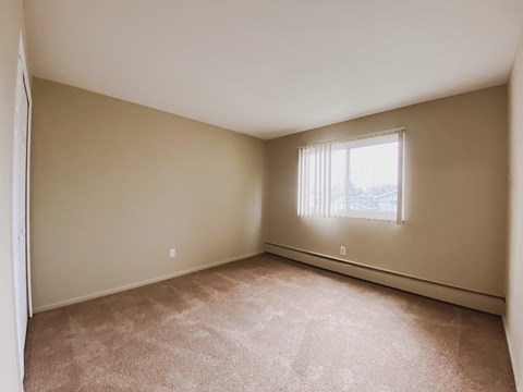 an empty bedroom with a window and carpeting