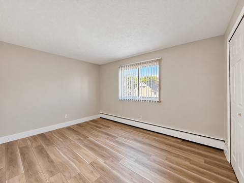 A room with wooden flooring and a window with blinds.