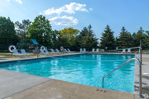 A large swimming pool surrounded by trees and lounge chairs.
