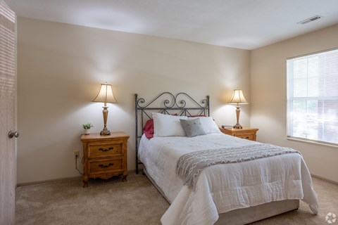 A bedroom with a bed, nightstands, and lamps. at Highlands of Heritage Woods Apartments, Copley