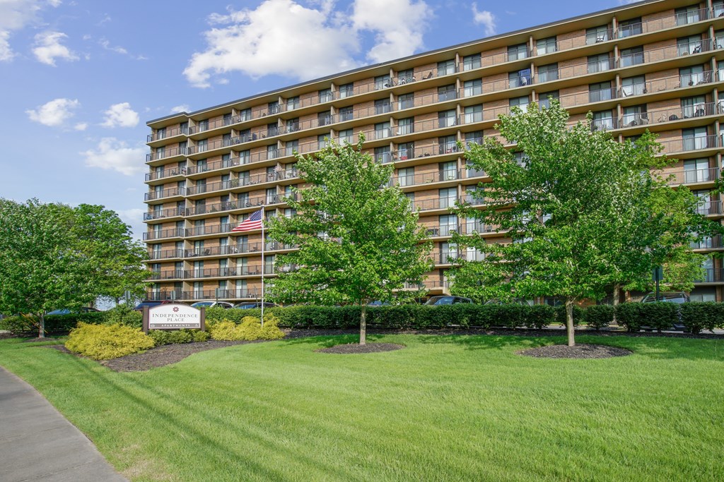 A large apartment building with a lawn in front and a sign that says at Independence Place Apartments, Parma Heights, 44130