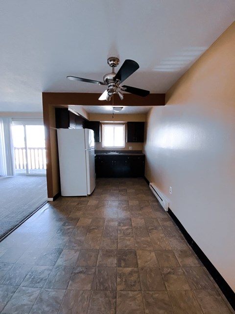 an empty living room with a ceiling fan and a refrigerator