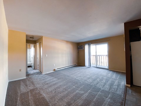 the living room of an empty apartment with a carpeted floor and a balcony