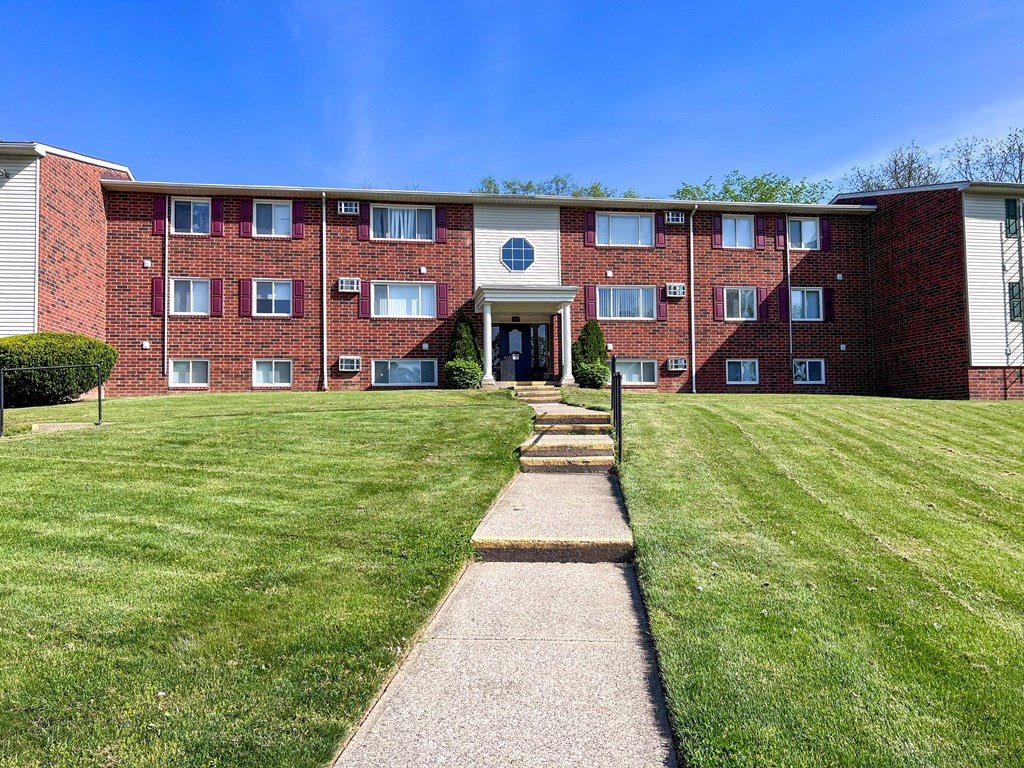 a large brick apartment building with a lawn and sidewalk