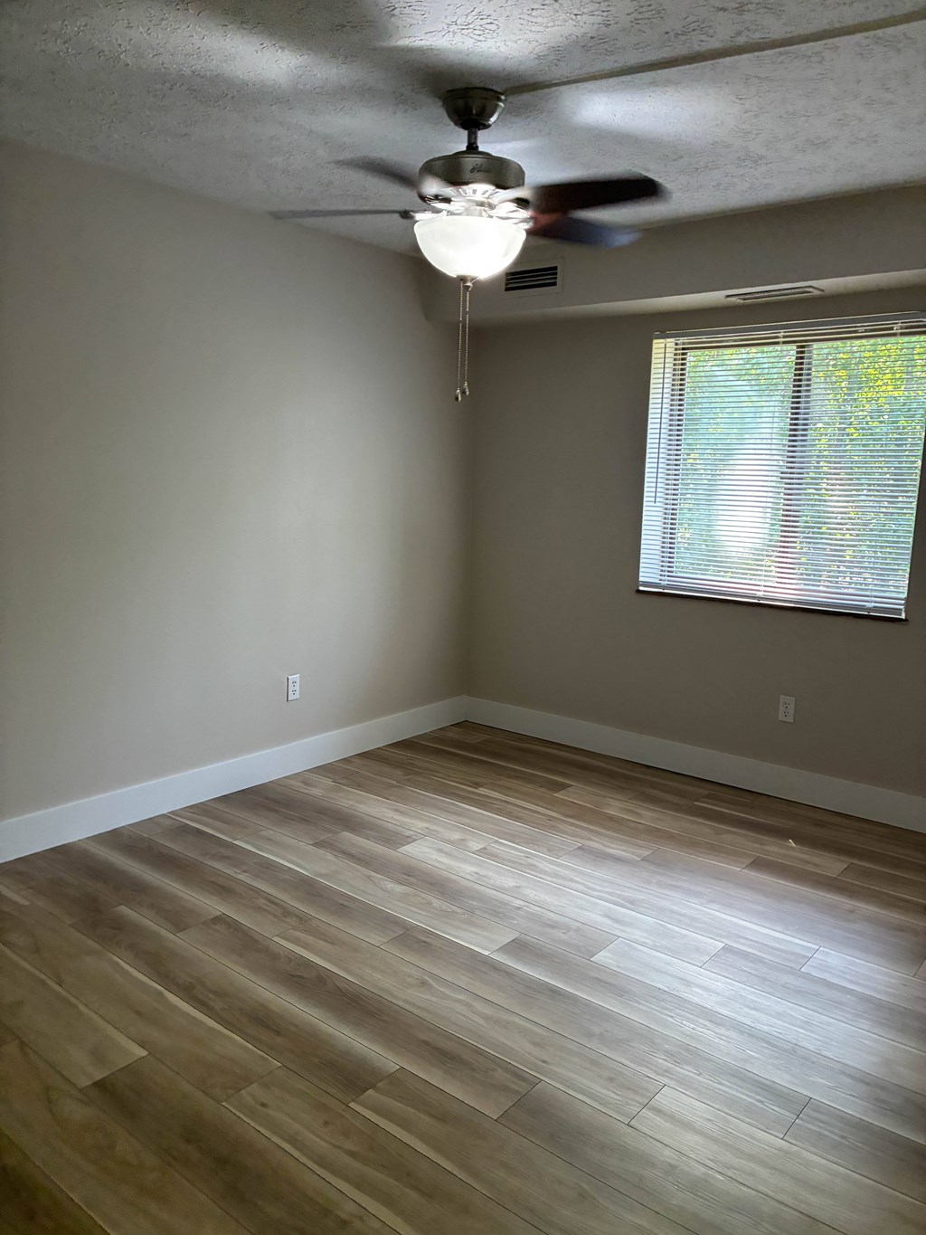 A room with a ceiling fan and a window with blinds.