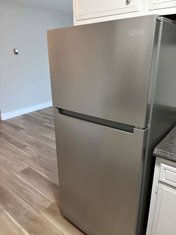 A stainless steel refrigerator in a kitchen with wooden flooring.