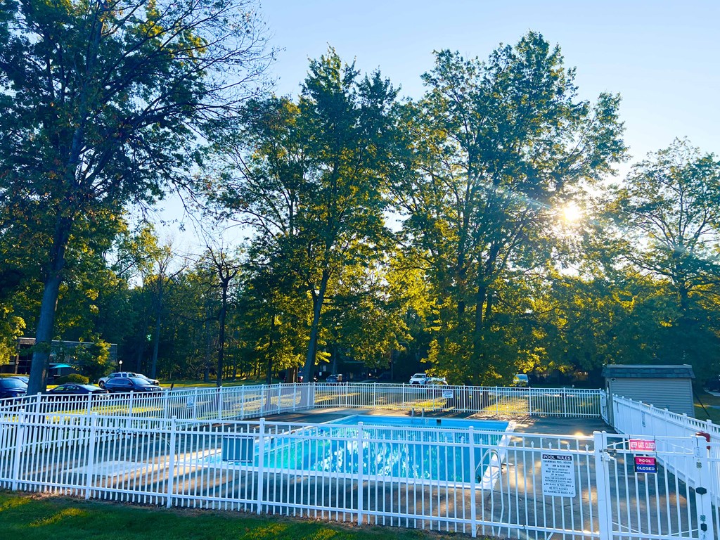 A pool surrounded by a white fence with trees in the background.