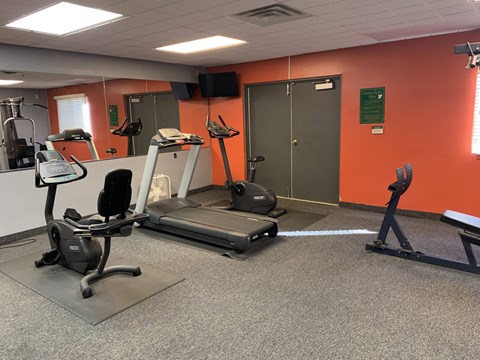A gym with orange walls has a treadmill, elliptical trainer, and a stationary bike.
