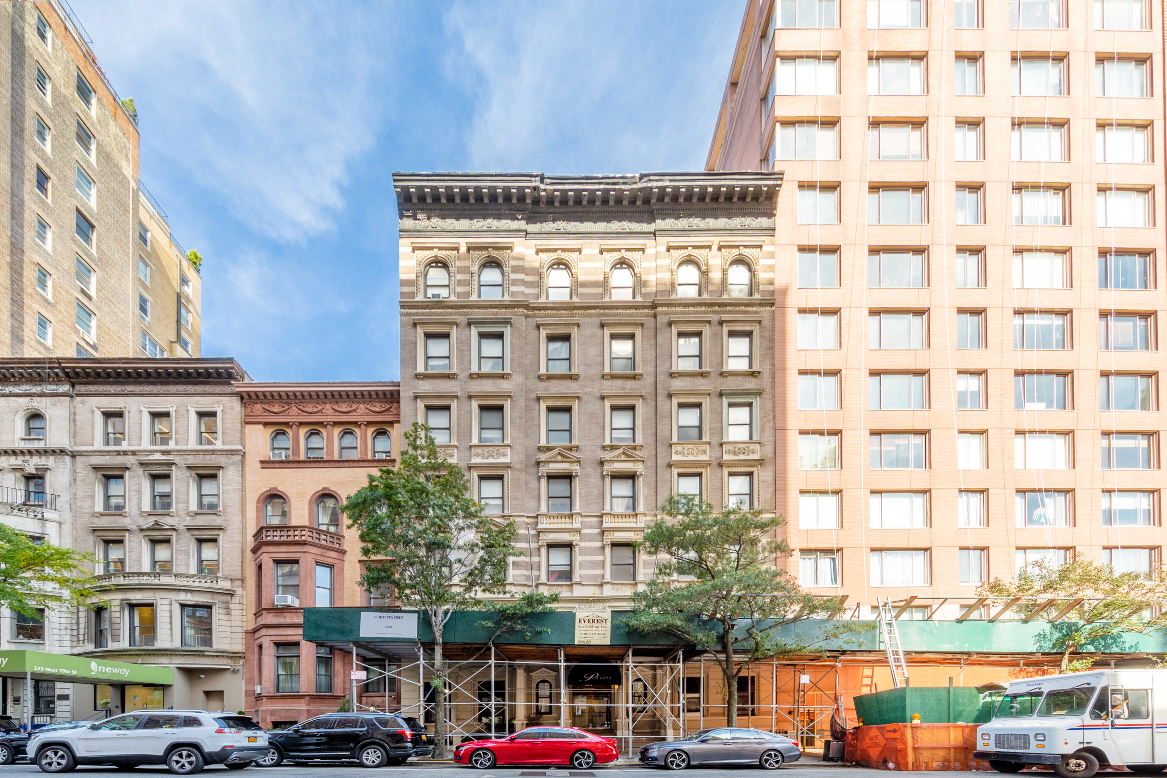 A red car is parked in front of a building with a green awning.