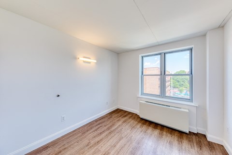 a bedroom with white walls and a window and wood floors