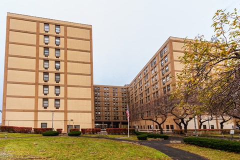 Two tan buildings with windows and a flag in front of them.
