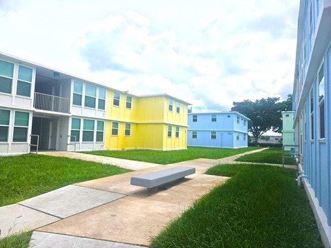 A building with a blue and yellow exterior is surrounded by a grassy area and a concrete walkway.