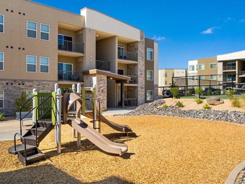 A playground with a slide and a climbing frame in front of apartment buildings.