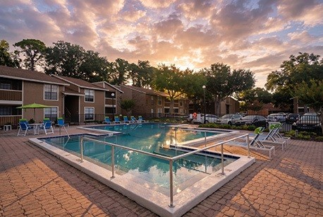 A swimming pool surrounded by a brick patio and chairs.