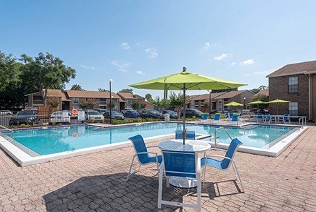 A pool area with a table and chairs and a green umbrella.