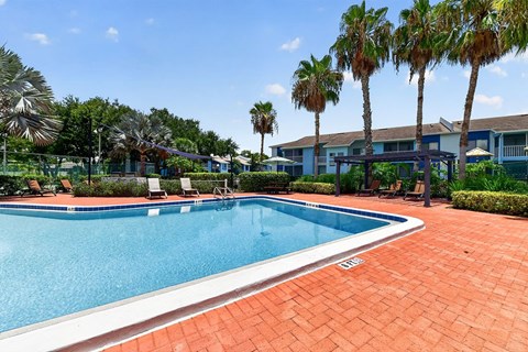 A swimming pool surrounded by palm trees and a brick patio.