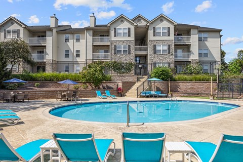 A large apartment complex with a pool and lounge chairs.
