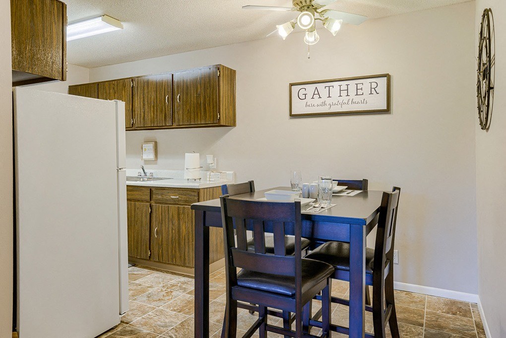 a dining area with a table and chairs and a kitchen with a refrigerator