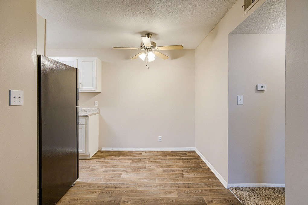 an empty living room with a ceiling fan and a kitchen