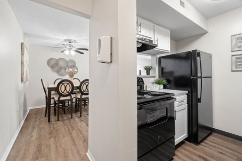 A kitchen with a black refrigerator and a dining table with chairs.