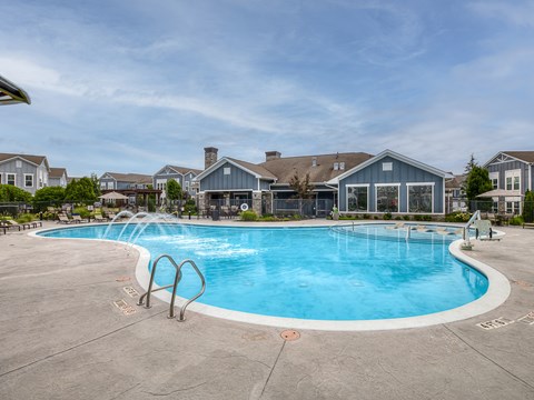 A large outdoor swimming pool surrounded by a concrete patio and residential buildings.