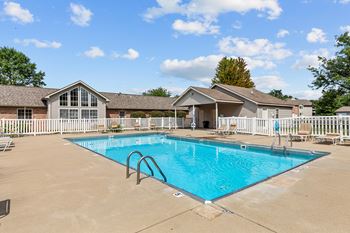 A swimming pool in front of a house with a white fence.