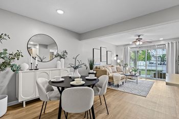 A modern dining room with a round mirror, a dining table with chairs, and a living area with a sofa.