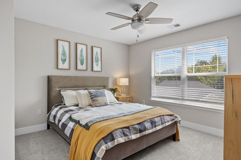 A bedroom with a bed, a ceiling fan, and two framed pictures on the wall.