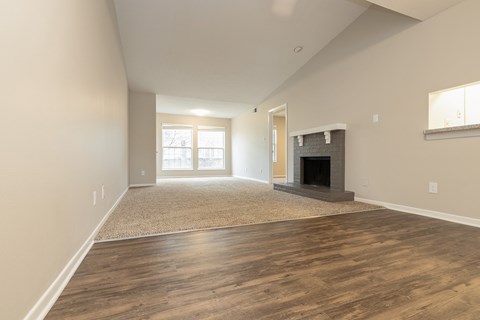 A large living room featuring a fireplace, beige carpeting, bright windows, and a vaulted ceiling.