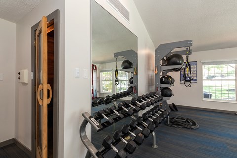 A gym with a mirror, weights, and other equipment, featuring a sauna around the corner.